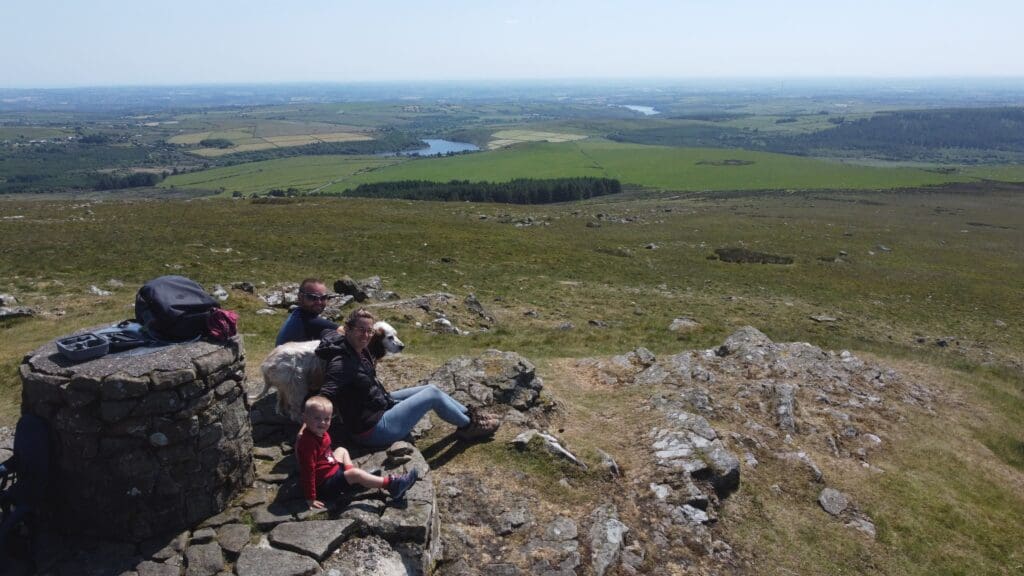 Famille assise sur un promontoire rocheux avec un chien, sur les hauteurs d’un paysage vallonné du Pays de Galles, vue aérienne par drone.