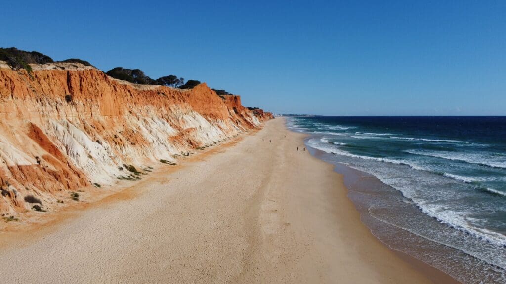 Falaises ocre de la plage des Trois Frères en Algarve, avec longue plage de sable et vagues de l’océan Atlantique, vue aérienne par drone.