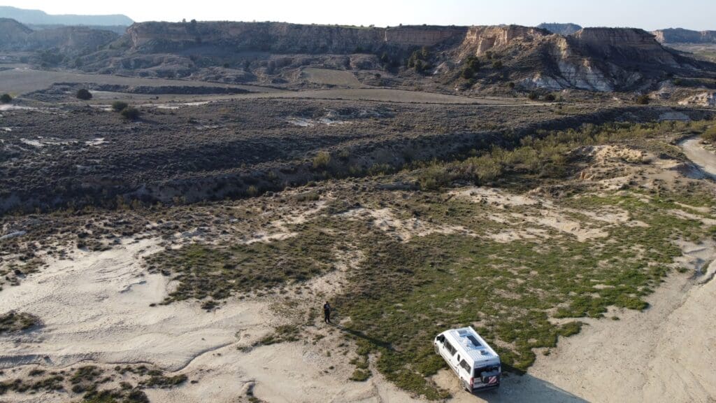 Van aménagé stationné dans le désert de Gorafe en Espagne, avec paysages arides, reliefs érodés et falaises ocres en arrière-plan, vue aérienne par drone.