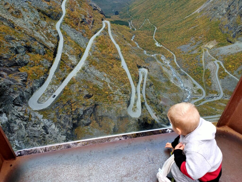 Enfant observant la route des Trolls en Norvège, une route de montagne en lacets vue depuis un belvédère lors d’un voyage en van en famille.