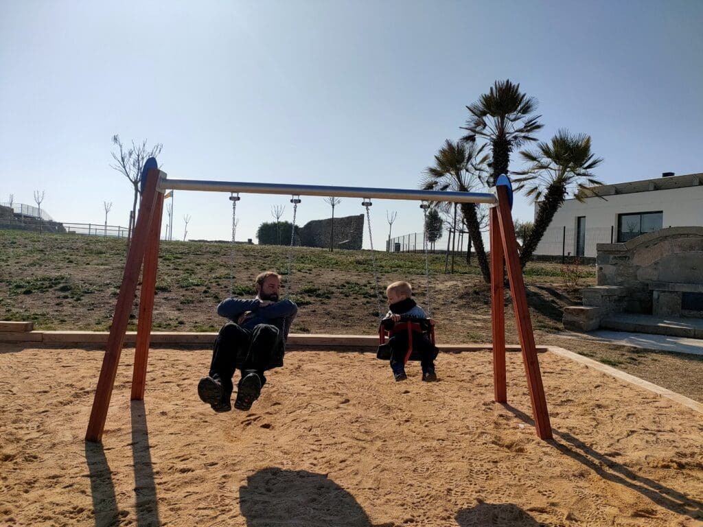 Papa et Tom assis sur des balançoires dans une aire de jeux en Espagne, pendant l’attente d’une lessive en laverie lors d’un voyage en van.