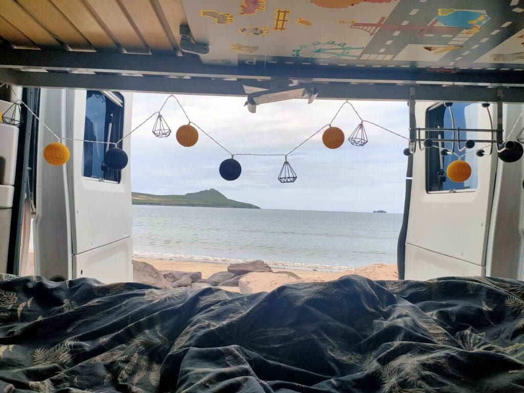 Vue depuis le lit du van, porte arrière ouverte sur une plage d'Irlande au lever du matin — vanlife SED Aventures