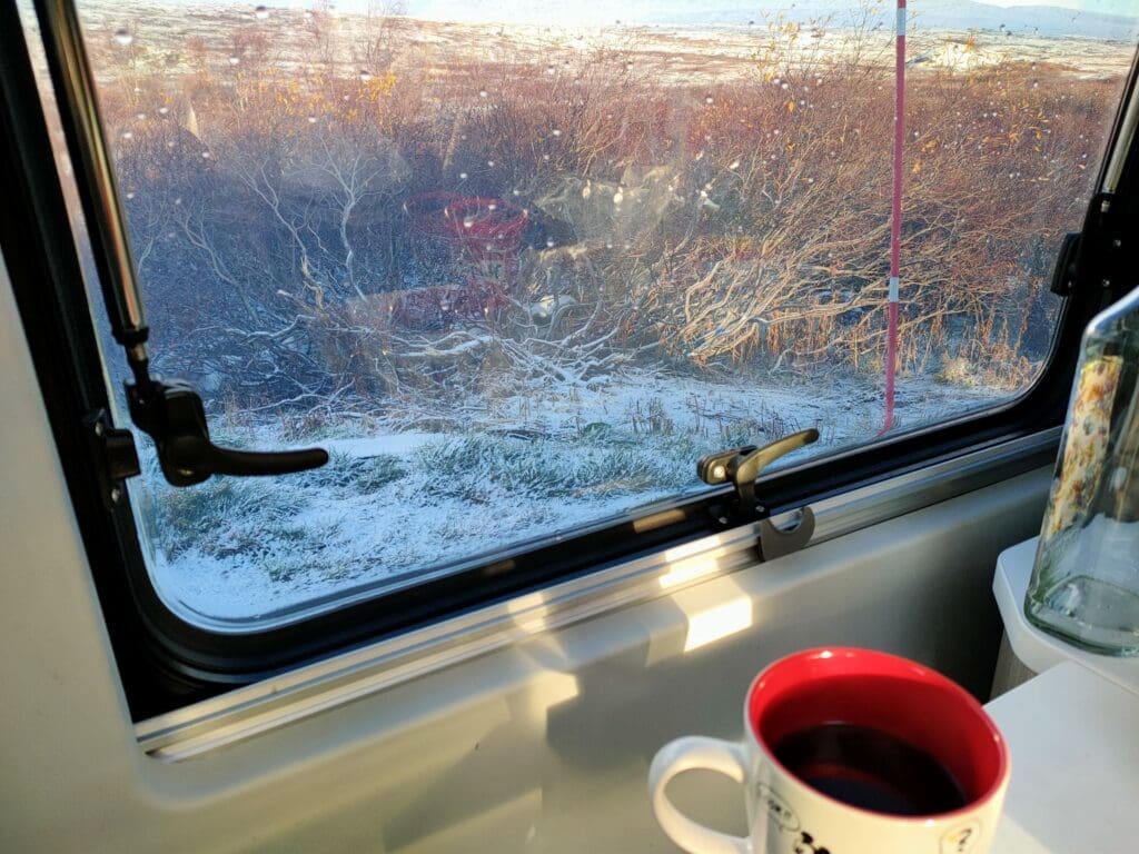 Vue depuis l'intérieur du van sur un paysage enneigé au cercle polaire en Norvège, tasse de café au premier plan, ambiance slow travel hivernal