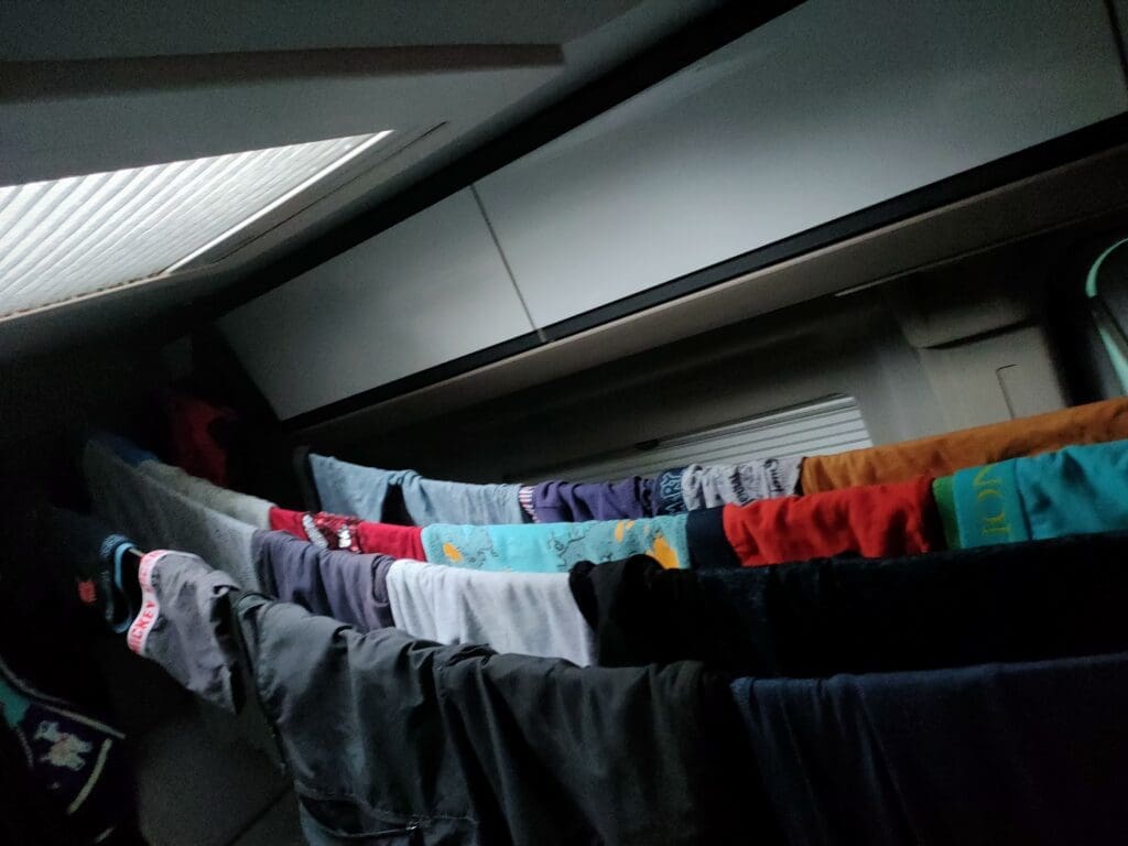 Linge de famille étendu à sécher à l'intérieur du van après une panne de sèche-linge en camping — réalité vanlife