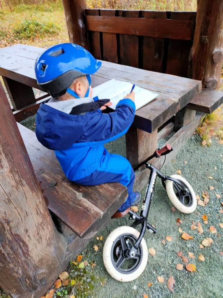 Tom dessine dans un livre d'or après une randonnée, casque de vélo sur la tête — roadschooling en pleine nature