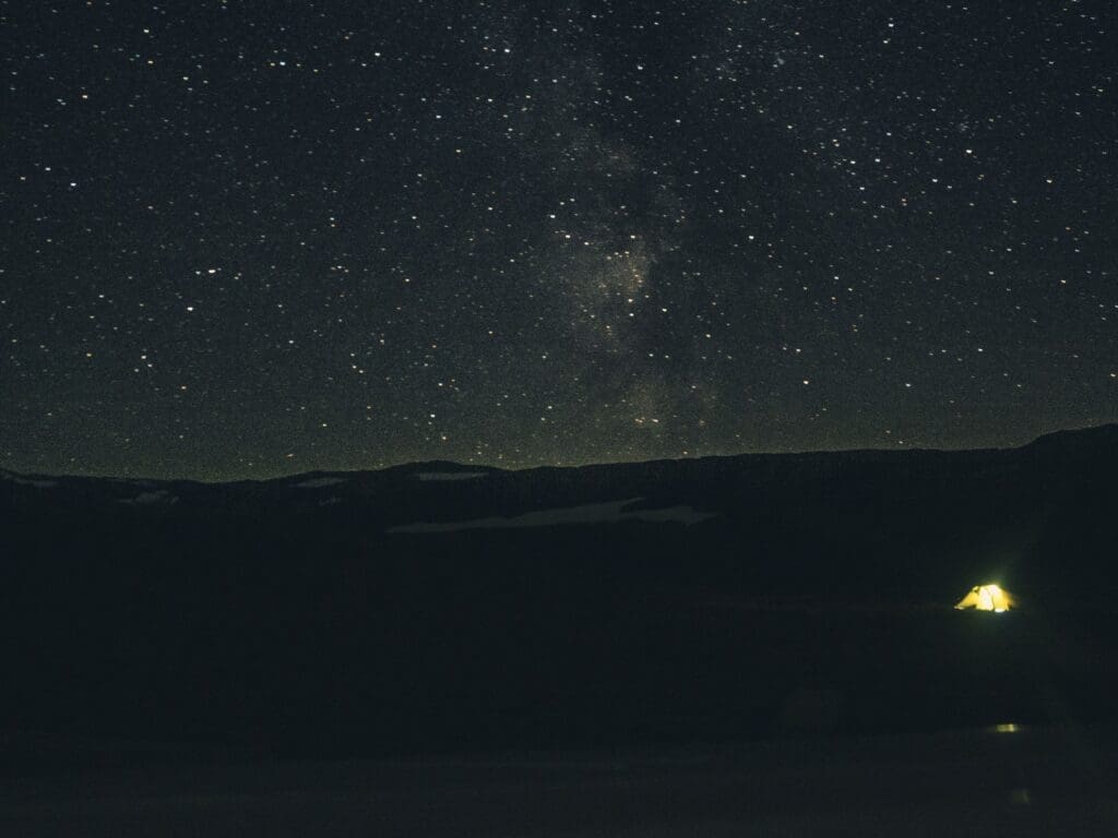 Ciel étoilé avec la Voie Lactée visible au-dessus d'un sommet enneigé en Norvège, tente isolée dans l'obscurité — nuit vanlife hors réseau
