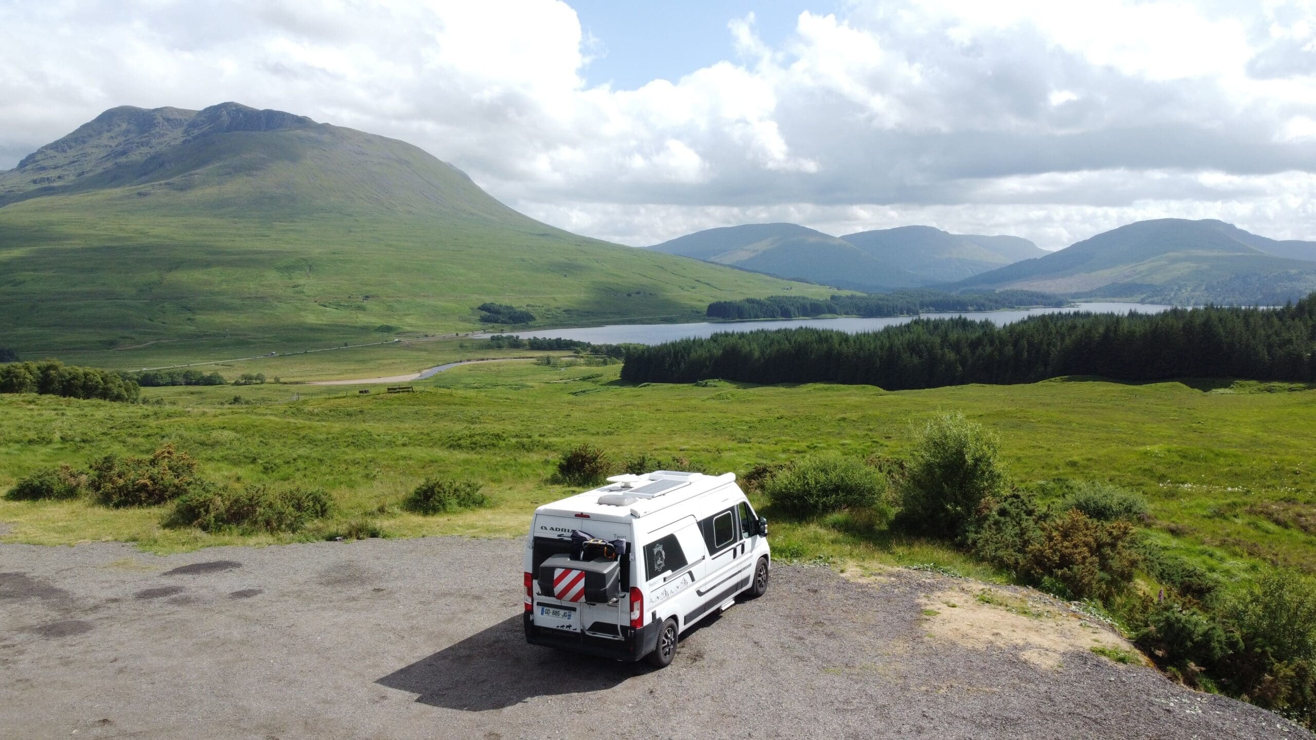 Van aménagé SED Aventures stationné face à un loch écossais entouré de collines verdoyantes, pause déjeuner en road trip en Écosse