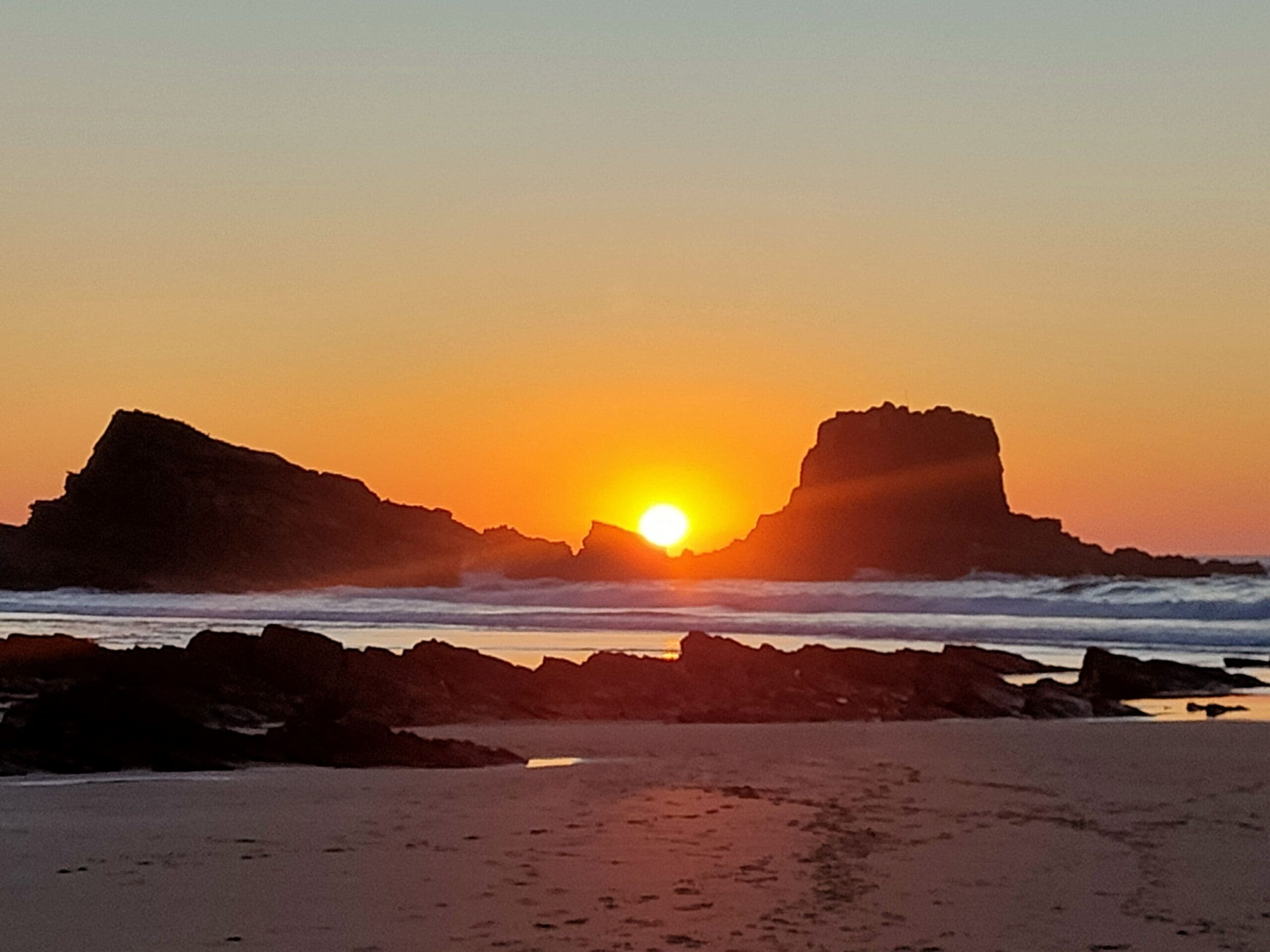 Coucher de soleil orangé entre deux rochers sur une plage sauvage du sud du Portugal — road trip vanlife en famille