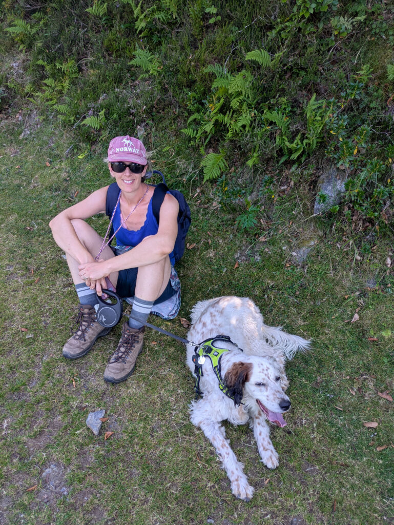 Milky allongée au repos pendant une pause de randonnée avec sa maîtresse dans une zone végétalisée.