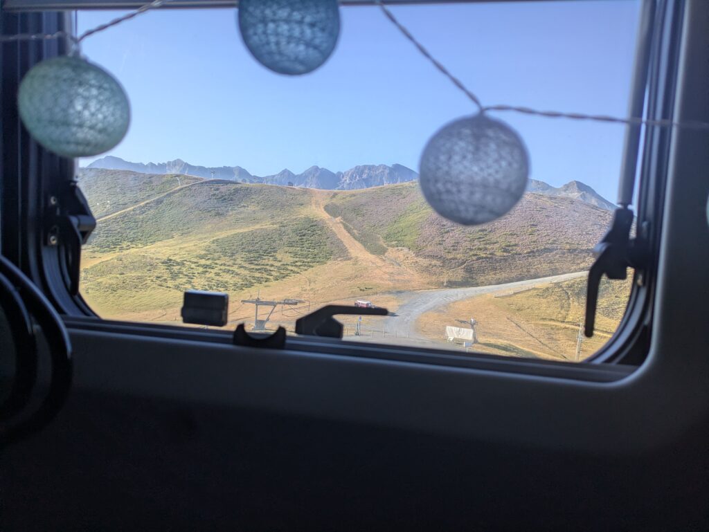 Vue sur les montagnes depuis le lit à l’intérieur d’un van aménagé, avec la fenêtre donnant sur le paysage.
